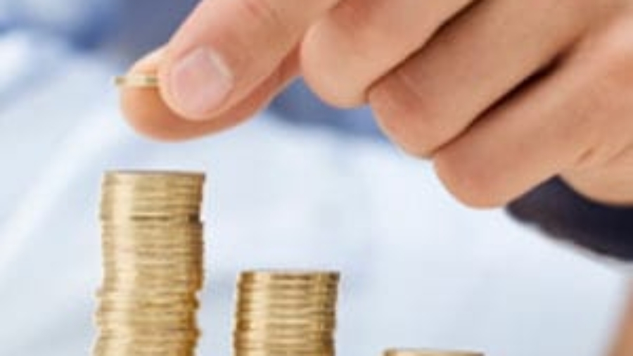 Hand placing a coin on top of small growing stacks of gold coins
