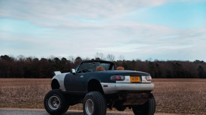 Modified convertible car with oversized off-road wheels parked outdoors near an open field