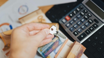 Hand holding a silver key over financial documents, cash banknotes, and a calculator