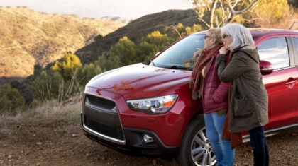 Two senior women leaning against a red SUV on a scenic mountain overlook