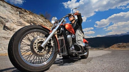 Motorcycle rider wearing a helmet riding a orange cruiser motorcycle on an open road against a blue sky