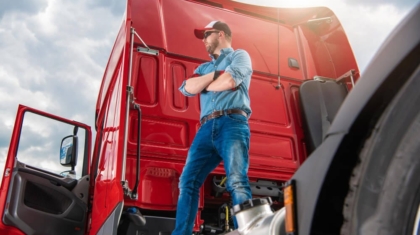 Truck driver wearing a cap standing next to the cabin of a large red semi-truck