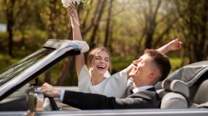 Newlywed couple cheering in a convertible car with the bride holding up her bouquet