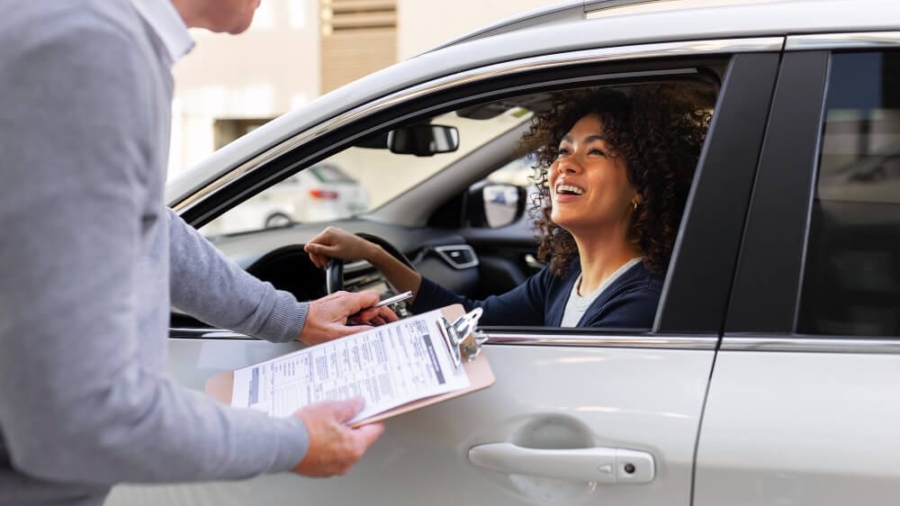 Insurance agent handing a clipboard with paperwork through a car window to a smiling female driver