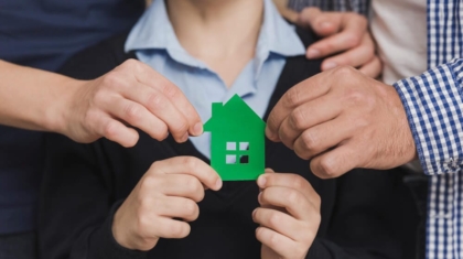 Family hands holding a green paper house cutout together