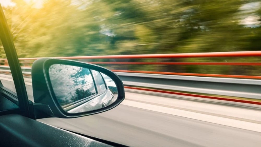 Car side mirror view driving along a highway with motion blur on the trees