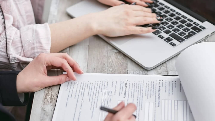 Two professionals reviewing a printed commercial insurance form while typing on a laptop keyboard at a desk