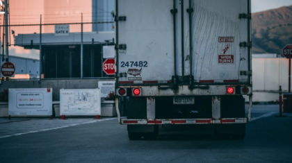 Rear view of a white semi-truck trailer parked in front of an industrial facility with stop signs