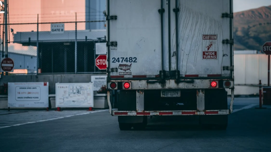 Rear view of a white semi-truck trailer parked in front of an industrial facility with stop signs
