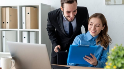 Male manager and female employee smiling while looking at documents on a clipboard in an office setting