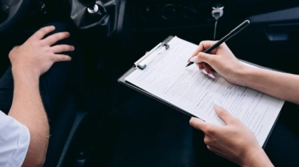 Hands filling out an insurance discount checklist on a clipboard inside a car