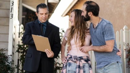 Insurance agent holding a clipboard while reviewing a home insurance claim with a young couple outside their house