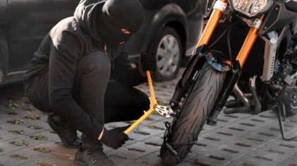 Person wearing a ski mask attempting to break a motorcycle wheel lock outdoors