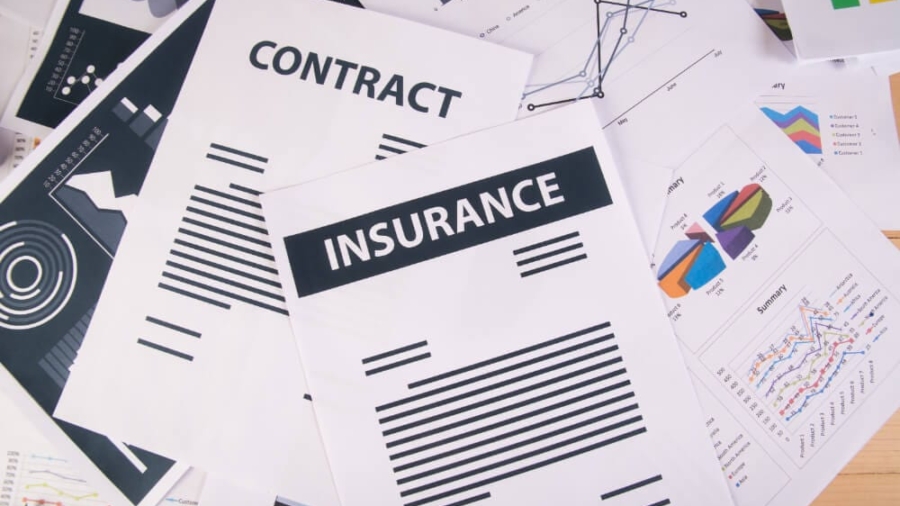 Scattered auto insurance policy contracts, financial charts, and rate documents on a desk