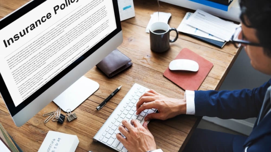 Person typing on a keyboard at a wooden desk with an auto insurance policy displayed on a computer screen