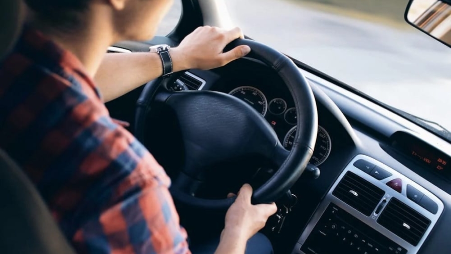 Driver holding the steering wheel inside a car while driving on a road