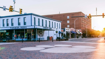 Street view of Toomer's Drugs at a sunlit intersection with traffic lights in Auburn, Alabama